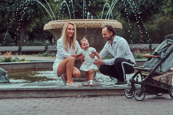 Mutlu aile kavramı - küçük kızları yakınındaki çeşmeden parkta poz ile iki genç ebeveyn.