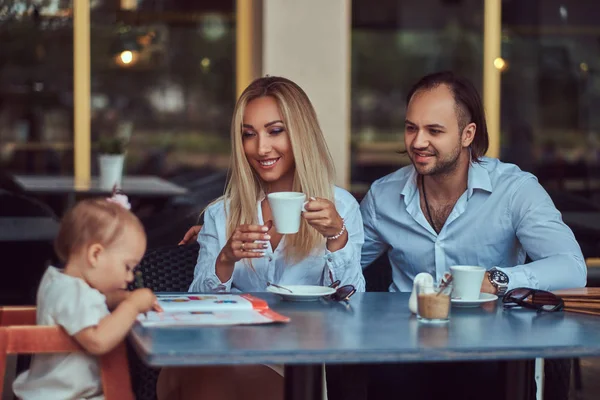 Beautiful blonde woman and handsome male enjoying family life with their little daughter in an outdoor cafe.