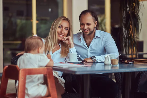 Beautiful blonde woman and handsome male during time with their little daughter in an outdoor cafe. Family and people concept.