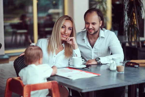 Beautiful blonde woman and handsome male during time with their little daughter in an outdoor cafe. Family and people concept.