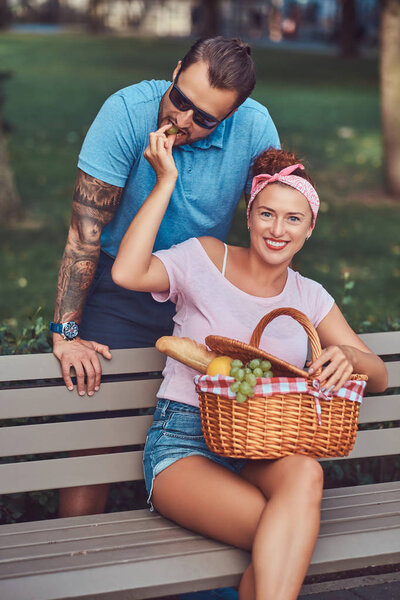 Attractive middle age couple during dating, enjoying a picnic on a bench in the park.