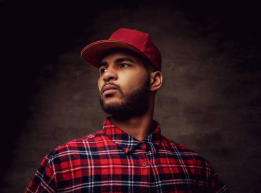 Bir kırmızı Polar gömlek ve cap adlı stüdyo bir Afrikalı-Amerikalı hipster adam portresi giymiş. Karanlık dokulu bir arka plan üzerinde izole.