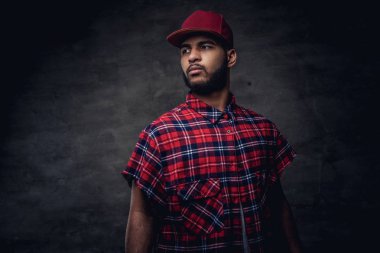 Bir kırmızı Polar gömlek ve cap adlı stüdyo bir Afrikalı-Amerikalı hipster adam portresi giymiş. Karanlık dokulu bir arka plan üzerinde izole.