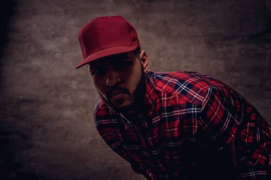 Bir kırmızı Polar gömlek ve cap adlı stüdyo bir Afrikalı-Amerikalı hipster adam portresi giymiş. Karanlık dokulu bir arka plan üzerinde izole.