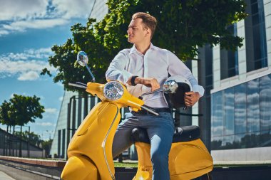 Emin yakışıklı şık saç kesimi ile beyaz bir gömlek, kot pantolon ve güneş gözlüğü tutar kask ve bir gökdelen karşı sarı klasik İtalyan scooter üzerinde oturan giymiş.