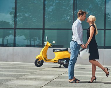 Aşık - şık yakışıklı beyaz tişört ve kot pantolon ve siyah elbise giyen sevimli sarışın kadın giymiş güzel çift el ele tutuşup karşı bir gökdelen öp.