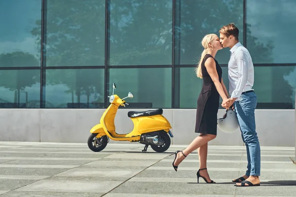 Aşık - şık yakışıklı beyaz tişört ve kot pantolon ve siyah elbise giyen sevimli sarışın kadın giymiş güzel çift el ele tutuşup karşı bir gökdelen öp.