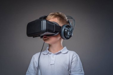 Bir okul çocuğu yakın çekim portre bir stüdyoda bir sanal gerçeklik bardaklarda beyaz bir t-shirt ayakta giymiş. Gri bir arka plan üzerinde izole.