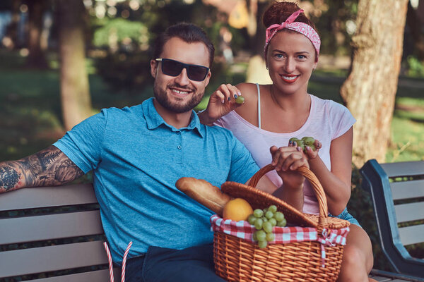 Attractive middle age couple during dating, enjoying a picnic on a bench in the park.