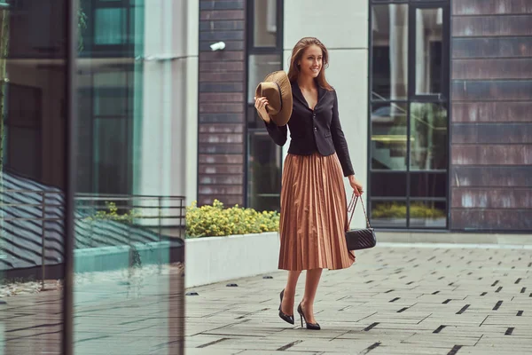 Moda feliz mulher elegante vestindo uma jaqueta preta, chapéu marrom e saia com uma embreagem bolsa andando no centro da cidade europeia . — Fotografia de Stock