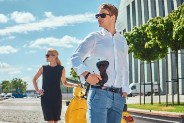 Beyaz tişört ve kot pantolon ve siyah elbise ayakta bir sarı klasik İtalyan scooter yakınındaki bir gökdelen karşı giyen sevimli sarışın kadın çekici çift - yakışıklı olan şık giyinmiş. Tatil ve insanlar kavramı.