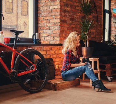 Uzun kıvırcık saçlı bir polar gömlek ve çatı iç bir stüdyoda bir ahşap kutu üzerinde otururken bir kamera ile kot giymiş çekici sarışın hippi kız.