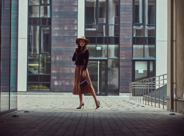 Мода елегантна жінка, що носить чорна куртка, коричнева капелюх і спідниця з сумочкою зчеплення ходіння по центру європейського міста. — стокове фото