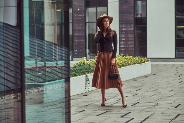 Moda mulher elegante vestindo uma jaqueta preta, chapéu marrom e saia com uma embreagem bolsa andando no centro da cidade europeia . — Fotografia de Stock