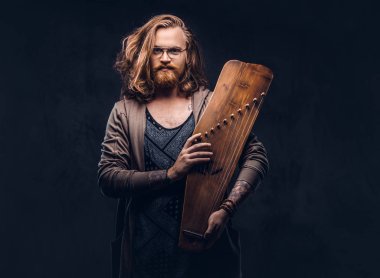 Kızıl saçlı hippi erkek uzun gür saçlı ve tam sakal içinde rahat kıyafetler giymiş bir Rus geleneksel müzik aleti - gusli tutar. Karanlık bir arka plan üzerinde izole. 