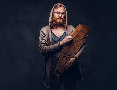 Kızıl saçlı hippi erkek uzun gür saçlı ve tam sakal bir hoodie giyinmiş ve t-shirt bir Rus geleneksel müzik aleti - gusli tutar. Karanlık bir arka plan üzerinde izole. 