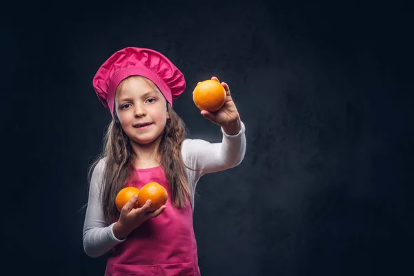 穿着粉红色厨师制服的可爱漂亮的女生在画室里放橘子 在深色纹理背景下隔离 — 图库照片