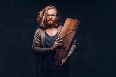 Kızıl saçlı hippi erkek uzun gür saçlı ve tam sakal içinde rahat kıyafetler giymiş bir Rus geleneksel müzik aleti - gusli tutar. Karanlık bir arka plan üzerinde izole. 