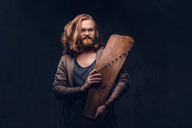 Kızıl saçlı hippi erkek uzun gür saçlı ve tam sakal içinde rahat kıyafetler giymiş bir Rus geleneksel müzik aleti - gusli tutar. Karanlık bir arka plan üzerinde izole. 