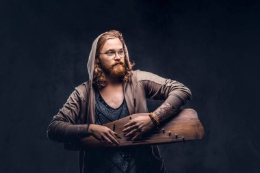 Kızıl saçlı hippi erkek uzun gür saçlı ve tam sakal hoodie ve bir Rus geleneksel müzik aleti - gusli üzerinde çalma t-shirt giymiş. Koyu arka plan üzerinde izole. 