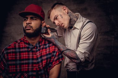 Yakışıklı sakallı Afrikalı-Amerikalı adam bir polar gömlek ve bir saç kesimi eski moda bir profesyonel kuaför tarafından getting kap bir saç kesimi yapıyor.