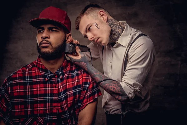 Yakışıklı sakallı Afrikalı-Amerikalı adam bir polar gömlek ve bir saç kesimi eski moda bir profesyonel kuaför tarafından getting kap bir saç kesimi yapıyor.