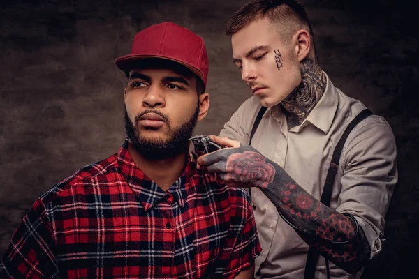 Yakışıklı sakallı Afrikalı-Amerikalı adam bir polar gömlek ve bir saç kesimi eski moda bir profesyonel kuaför tarafından getting kap bir saç kesimi yapıyor.