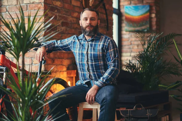Yakışıklı sakallı hippi erkek mavi Polar gömlek ve bir ahşap tabure çatı iç bir stüdyoda oturup kot.