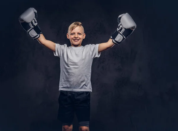 シャツ着てボクシング グローブに身を包んだ金髪陽気なハンサムな小さな少年ボクサーは 勝利に喜ぶ ダーク テクスチャ背景に分離 — ストック写真