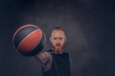Bir siyah spor top, karanlık dokulu bir arka plan üzerinde izole tutan bir kızıl saçlı basketbolcu portresi.