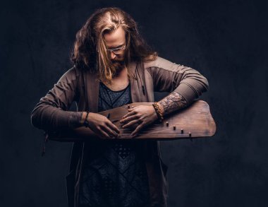 Kızıl saçlı hippi erkek uzun gür saçlı ve tam sakal bir Rus geleneksel müzik aleti - gusli üzerinde çalma rahat kıyafetler giymiş. Koyu arka plan üzerinde izole. 