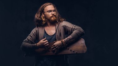 Kızıl saçlı hippi erkek uzun gür saçlı ve tam sakal bir Rus geleneksel müzik aleti - gusli üzerinde çalma rahat kıyafetler giymiş. Koyu arka plan üzerinde izole. 
