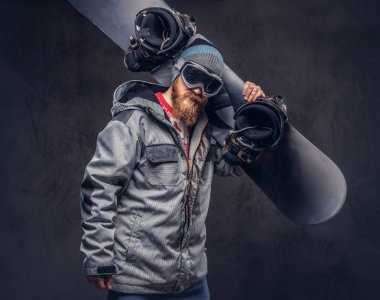 Bir kış şapka ve koruyucu gözlük bir snowboard ceket giymiş tam sakallı vahşi kızıl saçlı snowboard snowboard onun omuz bir stüdyoda tutar. Gri arka plan üzerinde izole.
