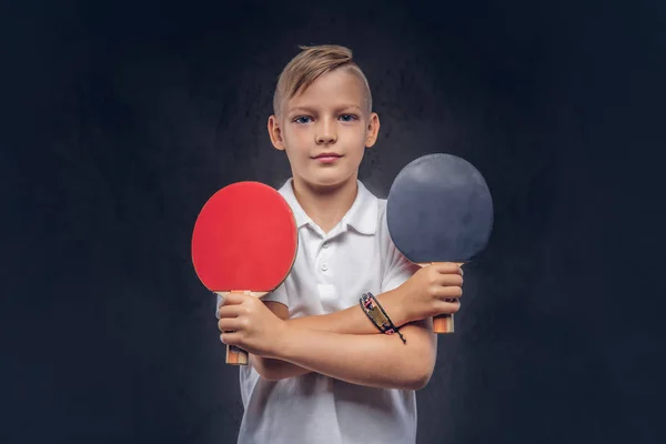 穿着白色 T恤衫的可爱男孩手持两只乒乓球球拍 在深色纹理背景下隔离 — 图库照片