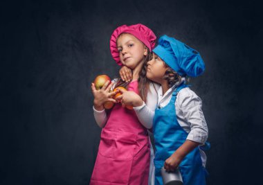 Portre sevimli iki küçük yemek yapıyor. Kahverengi kıvırcık saçlı küçük çocuk birlikte tutar tencere ve meyve bir stüdyoda sırasında sarılıyoruz pembe aşçı üniforma giymiş bir mavi aşçı düzgün ve güzel kız öğrenci giymiş. Bir karanlık dokulu bac izole