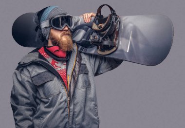Bir snowboard portresi extream snowboard snowboard yaparken omzunda bir stüdyoda ile poz tam koruyucu giysiler giymiş. Gri bir arka plan üzerinde izole.
