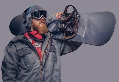 Bir snowboard portresi extream snowboard snowboard yaparken omzunda bir stüdyoda ile poz tam koruyucu giysiler giymiş. Gri bir arka plan üzerinde izole.