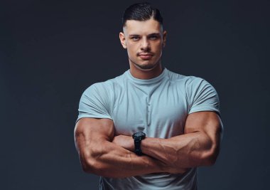 Spor giyim, ayakta bir kas yakışıklı vücut yakın çekim portre silah kameraya bakarak bir stüdyoda geçti. Gri bir arka plan üzerinde izole.