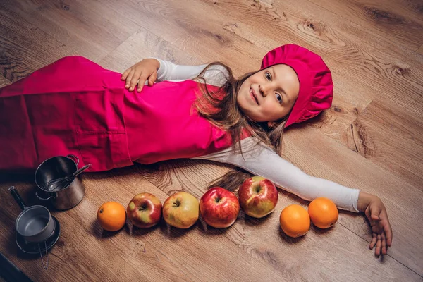 Bir pembe aşçı Tekdüzen bir ahşap yerde yatarken giyinmiş mutlu sevimli güzel kız öğrenci.