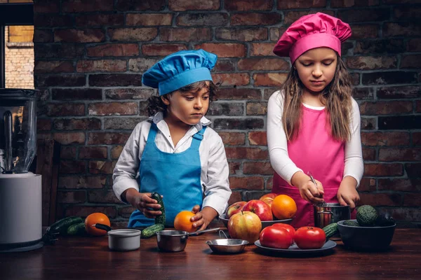 Sevimli aşçı çift. Mavi aşçı üniforma giymiş kahverengi kıvırcık saç ve güzel bir kız bir pembe giymiş olan küçük çocuk yemek Tekdüzen birlikte bir tuğla duvara bir mutfakta yemek.
