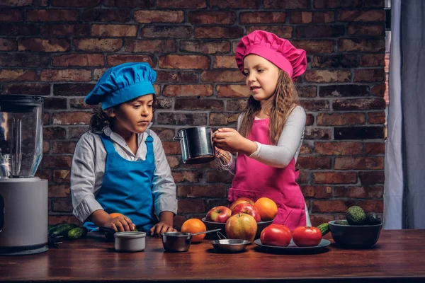 Sevimli aşçı çift. Mavi aşçı üniforma giymiş kahverengi kıvırcık saç ve güzel bir kız bir pembe giymiş olan küçük çocuk yemek Tekdüzen birlikte bir tuğla duvara bir mutfakta yemek.