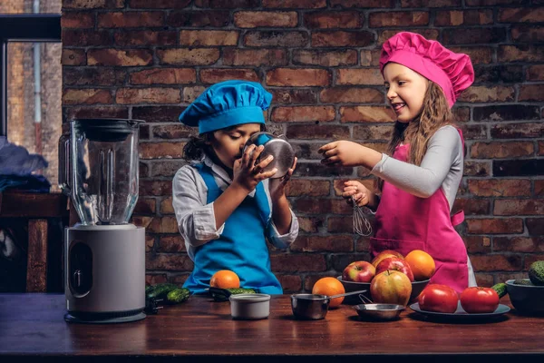 Sevimli aşçı çift. Mavi aşçı üniforma giymiş kahverengi kıvırcık saç ve güzel bir kız bir pembe giymiş olan küçük çocuk yemek Tekdüzen birlikte bir tuğla duvara bir mutfakta yemek.