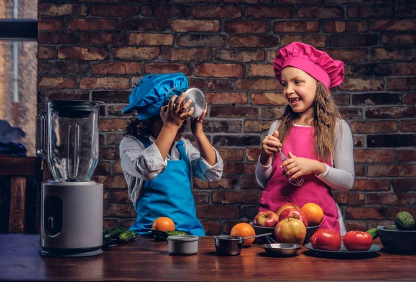 Sevimli aşçı çift. Mavi aşçı üniforma giymiş kahverengi kıvırcık saç ve güzel bir kız bir pembe giymiş olan küçük çocuk yemek Tekdüzen birlikte bir tuğla duvara bir mutfakta yemek.