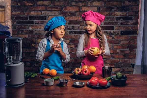 Sevimli aşçı çift. Mavi aşçı üniforma giymiş kahverengi kıvırcık saç ve güzel bir kız bir pembe giymiş olan küçük çocuk yemek Tekdüzen birlikte bir tuğla duvara bir mutfakta yemek.