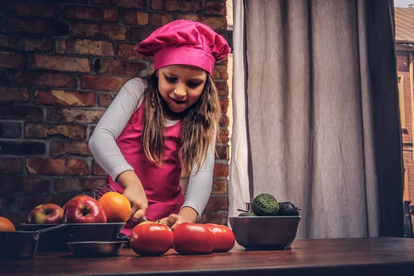Güzel kız öğrenci bir tuğla duvara bir mutfakta yemek pembe aşçı üniforma giymiş. — Stok fotoğraf