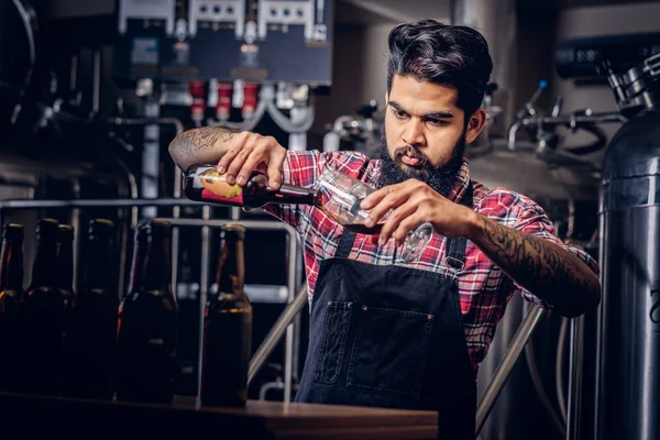 Kalite kontrol, arkasında, bira sayaç için bir bardak bira şık tam sakallı Hintli adam bir polar gömlek ve önlük dökülen.
