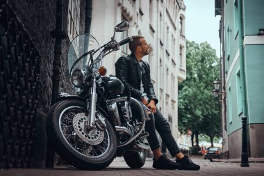 Bir siyah deri ceket ve retro motosikleti eski Avrupa sokakta oturan kot giymiş şık motorcu.