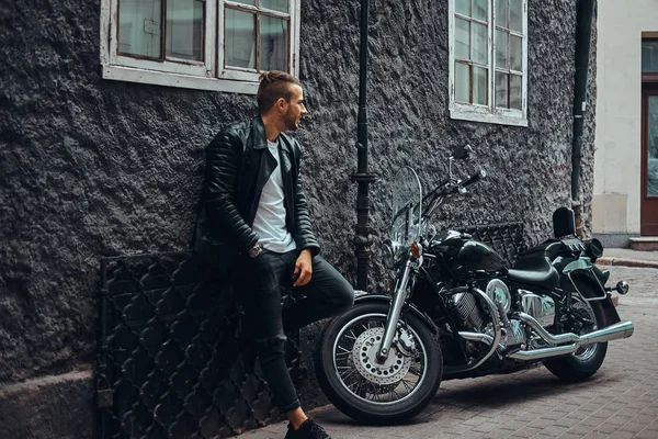 时尚的骑自行车穿着黑色的皮夹克和牛仔裤靠在墙附近 他的复古摩托车在旧欧洲街 — 图库照片