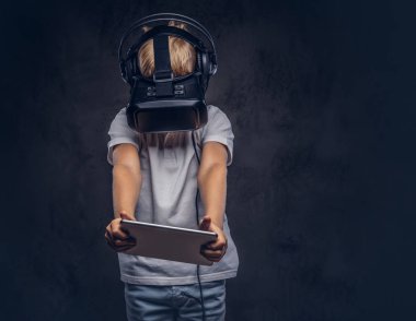 Liseli Sarışın sanal gerçeklik gözlük takan ve dijital tablet kullanma beyaz bir t-shirt giymiş. Karanlık dokulu bir arka plan üzerinde izole.