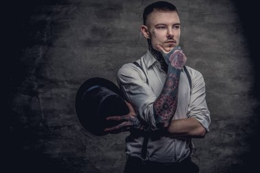 Beyaz gömlek ve pantolon askısı giyen düşünceli bir eski moda dövmeli adam portresi bir silindir şapka ve el çene üzerinde tutar. Karanlık bir arka plan üzerinde izole.